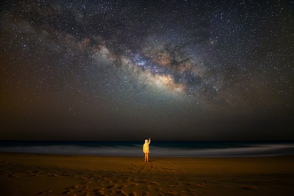 a person standing on a beach under a night sky