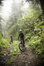 A group of adventurers riding mountain bikes along a lush forest trail near waterfalls.