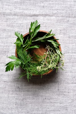 A bowl filled with coarse sea salt grains beside fresh herbs and spices