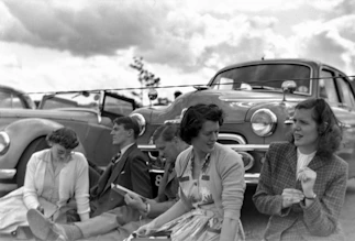 A group of friends gathered around a vintage car, sharing stories and laughter in a cozy garage setting.