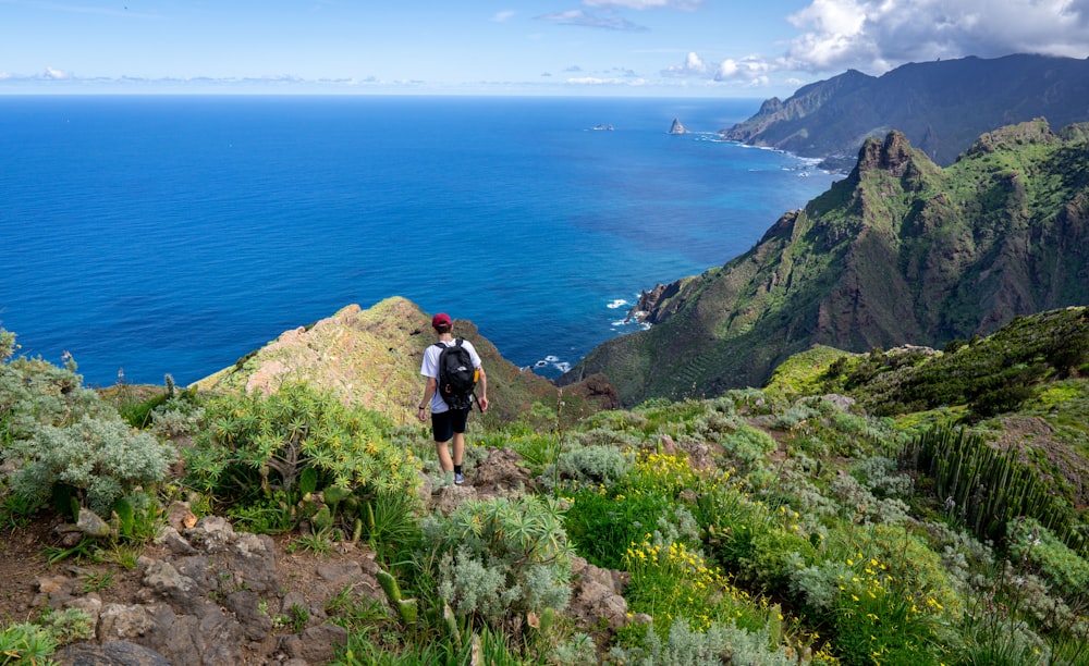 a man hiking up a mountain with the ocean in the background
