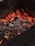 Red-hot charcoal embers glowing intensely, surrounded by black and grey burnt wood pieces within a dark container.