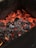 Red-hot charcoal embers glowing intensely, surrounded by black and grey burnt wood pieces within a dark container.