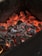 Red-hot charcoal embers glowing intensely, surrounded by black and grey burnt wood pieces within a dark container.