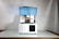 A 3D printer with a blue translucent cover is placed on a reflective surface. It has a rectangular base and an open chamber where the printing mechanism is visible. The power cord extends from the back and it is set against a plain background.