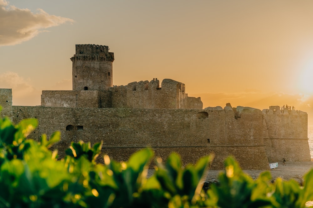 the sun is setting behind a castle by the water