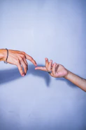 A close-up of two hands reaching through a barrier, fingers almost touching.