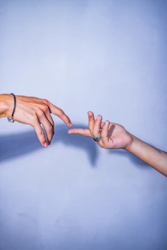 A close-up of two hands reaching through a barrier, fingers almost touching.