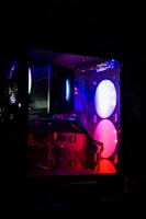 A computer tower with illuminated components and glowing LED lights. The interior reveals multiple components, such as fans and cables, with ambient lighting in shades of purple, blue, and pink.