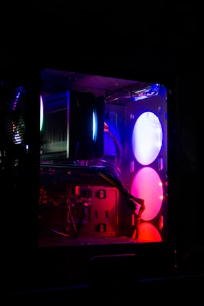 A computer tower with illuminated components and glowing LED lights. The interior reveals multiple components, such as fans and cables, with ambient lighting in shades of purple, blue, and pink.