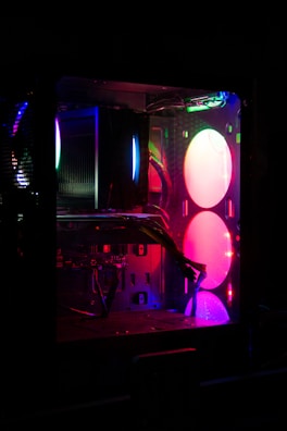 A computer case with visible internal components illuminated by vibrant RGB lighting. The colors include blue, red, and pink glowing lights that highlight the fans and hardware inside the case. The overall look is sleek and modern, emphasizing the aesthetics of gaming or high-performance PCs.