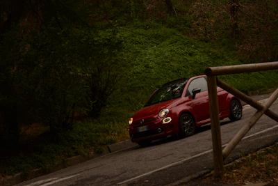 A compact car cruising along a winding mountain road surrounded by lush greenery.