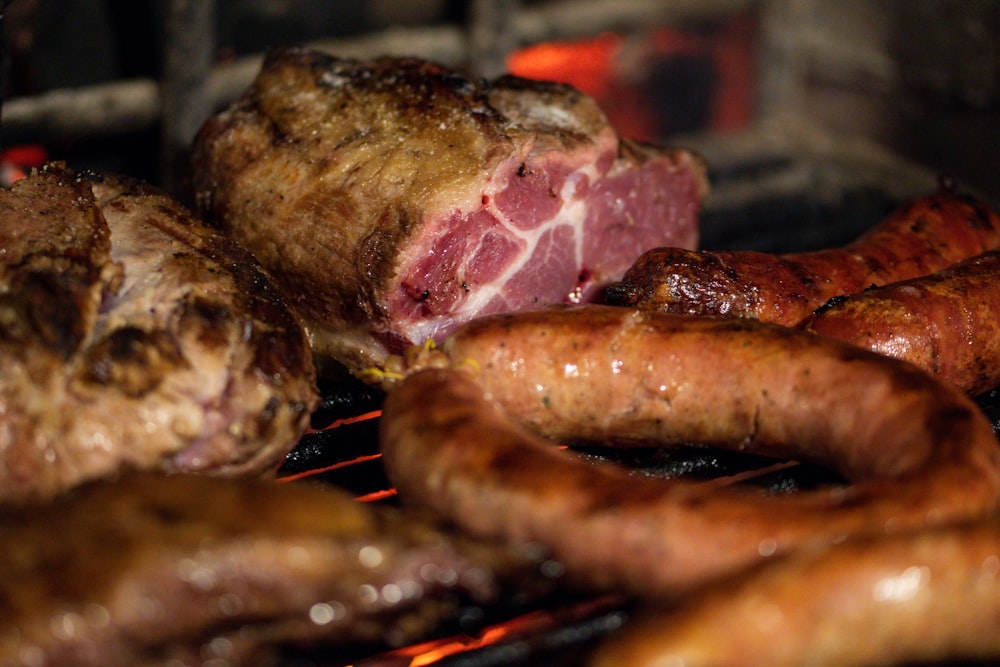 Un primer plano de carne y salchichas cocinando en una parrilla