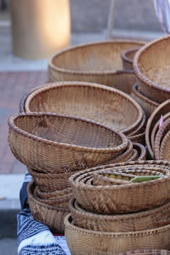 Several woven baskets are neatly stacked and displayed on a surface covered with a patterned fabric. The baskets vary in size but share a similar, natural brown color and are crafted with intricate patterns.