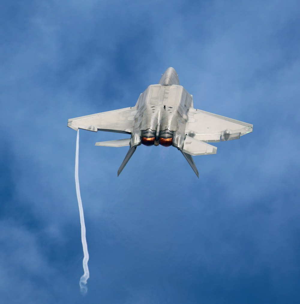a fighter jet flying through a blue cloudy sky