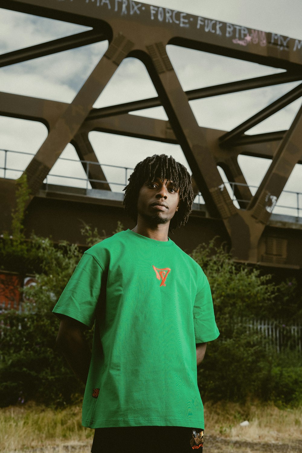 a man in a green shirt standing in front of a bridge