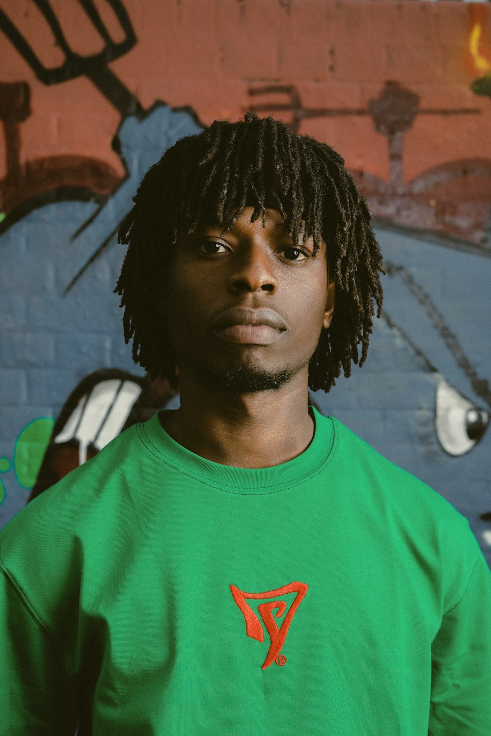 a man with dreadlocks standing in front of a wall