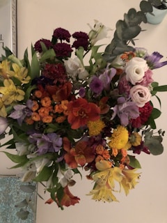 A vibrant bouquet of mixed flowers including roses, lilies, and orchids arranged in a clear vase.