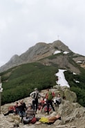 Group of hikers resting on a rocky outcrop overlooking a vast green valley.