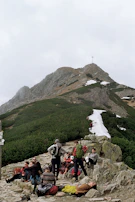 A group of hikers resting on rocky terrain, sharing stories with the mountain stretching behind them.