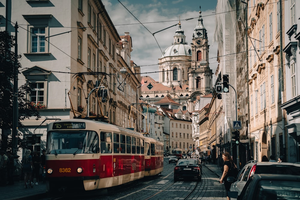 a red and white train traveling down a street next to tall buildings