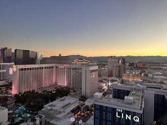 A cityscape view of Las Vegas at sunset, showcasing the skyline with prominent hotels and casinos. The sky displays a gradient of colors from dark blue to warm yellow as the sun sets in the background. Notable buildings are illuminated with lights, contributing to the vibrant nightlife atmosphere.