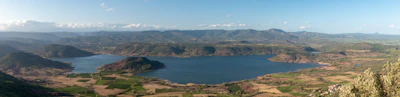 A panoramic shot of Mangla Lake shimmering under a clear blue sky, framed by rolling hills.