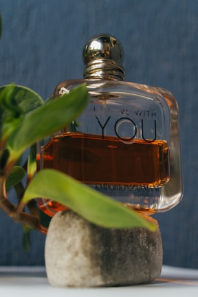 Close-up of a delicate glass perfume bottle resting on a bed of fresh green leaves.