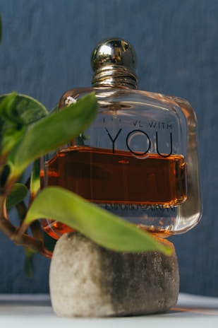 A close-up of a delicate glass perfume bottle resting on a bed of fresh citrus fruits and green leaves.