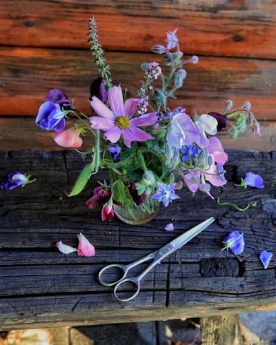 Close-up of a sunlit rustic wooden table adorned with freshly picked wildflowers in a simple glass jar.