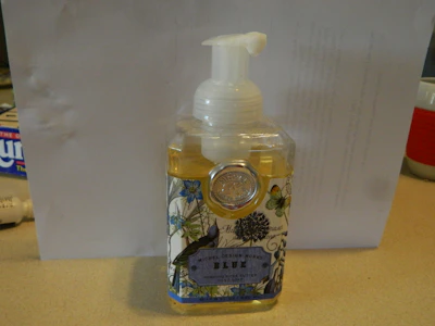 A clear bottle of hand wash with fresh flowers beside it on a bathroom counter