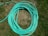 A coiled green garden hose lies on a patch of grass. The grass is mixed with dry, brown patches and lush green areas.