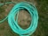 A coiled green garden hose lies on a patch of grass. The grass is mixed with dry, brown patches and lush green areas.