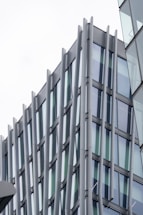 A modern architectural design featuring a building with glass windows and vertical metallic beams. The structure exhibits a sleek and contemporary style with reflective surfaces.