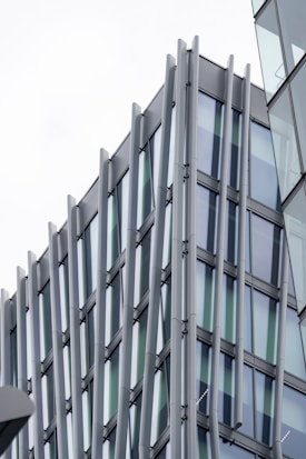 A modern architectural design featuring a building with glass windows and vertical metallic beams. The structure exhibits a sleek and contemporary style with reflective surfaces.