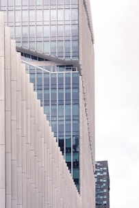 A modern high-rise building with a unique stepped architectural design featuring glass windows and beige paneling. The structure showcases a combination of vertical and diagonal lines, emphasizing a contemporary aesthetic.