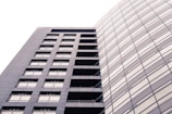 A modern, high-rise building with a sleek, rectangular design and numerous windows. The structure is composed of two distinct sections: one with visible balconies and another with a seamless glass facade. The lighting creates a soft, uniform tone across the building's exterior.