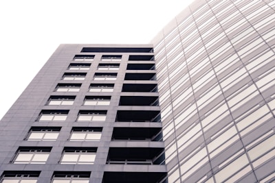 A modern, high-rise building with a sleek, rectangular design and numerous windows. The structure is composed of two distinct sections: one with visible balconies and another with a seamless glass facade. The lighting creates a soft, uniform tone across the building's exterior.