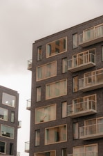 Modern apartment buildings with large windows and balconies. The structures have a sleek, contemporary design with dark brick exteriors.