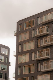 Modern apartment buildings with large windows and balconies. The structures have a sleek, contemporary design with dark brick exteriors.