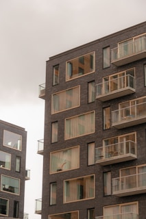 Modern apartment buildings with large windows and balconies. The structures have a sleek, contemporary design with dark brick exteriors.
