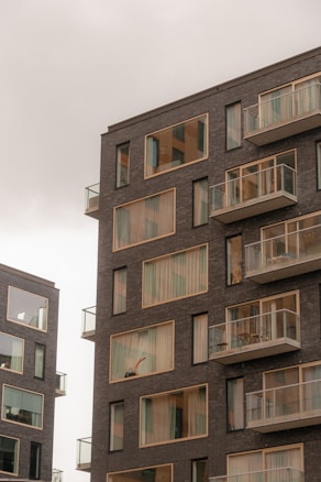 Modern apartment buildings with large windows and balconies. The structures have a sleek, contemporary design with dark brick exteriors.