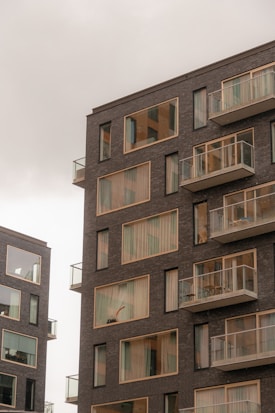 Modern apartment buildings with large windows and balconies. The structures have a sleek, contemporary design with dark brick exteriors.