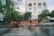 A group of workers wearing orange safety uniforms and helmets are cleaning a paved street area near a crosswalk. They are using hoses and brooms to clean the wet surface. Surrounding buildings, including a hotel named 'ROYAL HOTEL SAIGON,' and trees can be seen in the background.