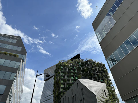 A cinematic shot of a drone filming a modern commercial building surrounded by greenery under a moody sky.