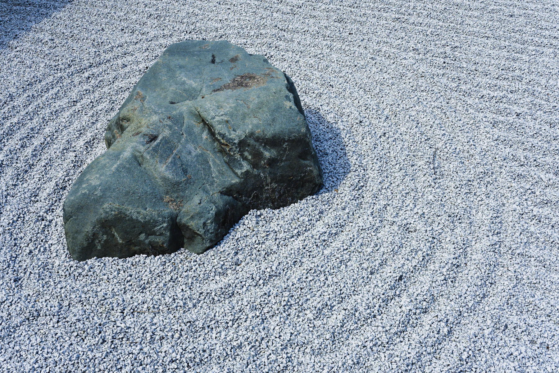 A blue-gray boulder set in rings of raked white gravel in a dry garden