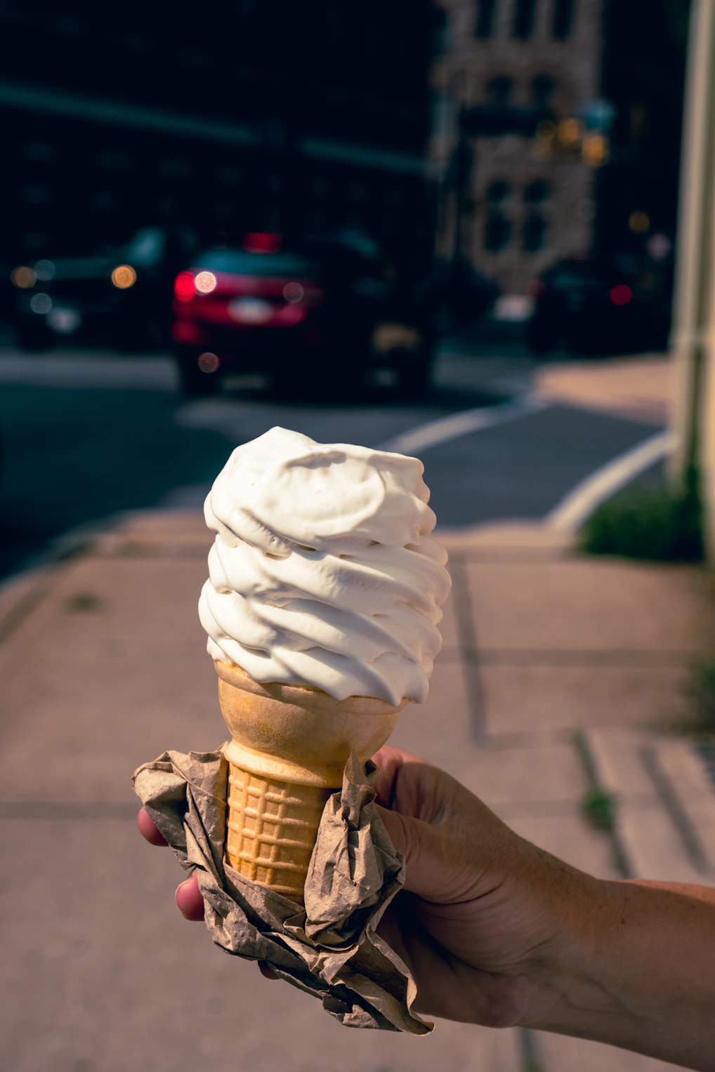 a hand holding an ice cream cone on a city street