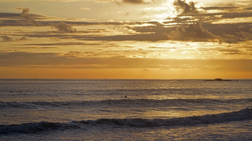 a person riding a surfboard in the ocean at sunset