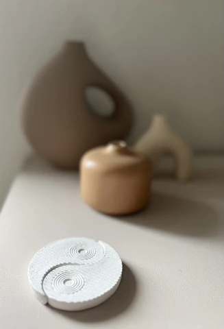 A series of minimalist ceramic pieces arranged in a grid, showcasing varied textures in monochrome tones.