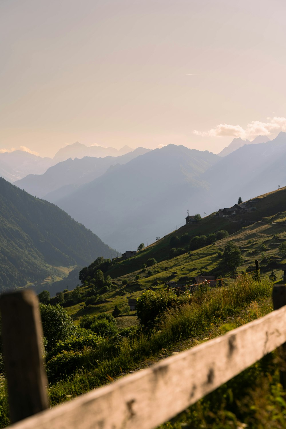 a wooden fence on a grassy hillside with mountains in the background